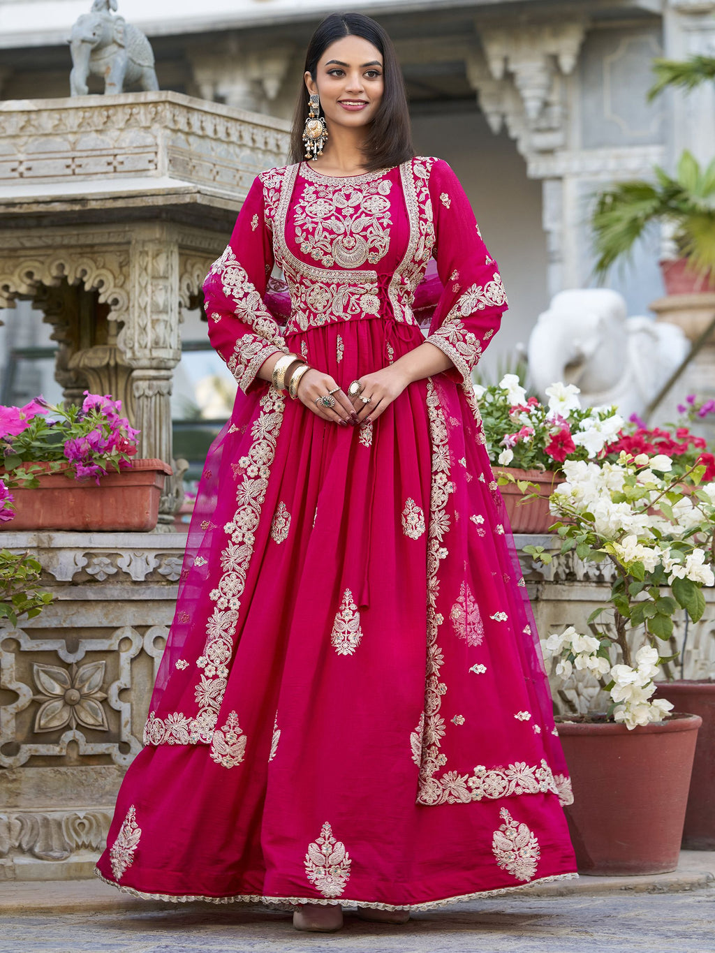 Anwitha Pink Embroidered Silk Anarkali Gown Set, crafted from luxurious Vichitra Silk with intricate sequins and thread embroidery accented by delicate lace details. This fully stitched Anarkali gown features a 3-meter flair and a soft cotton lining for comfort. Paired with a graceful net dupatta adorned with sequins embroidery and a lace border, this elegant ensemble is perfect for weddings, festive occasions, and grand celebrations