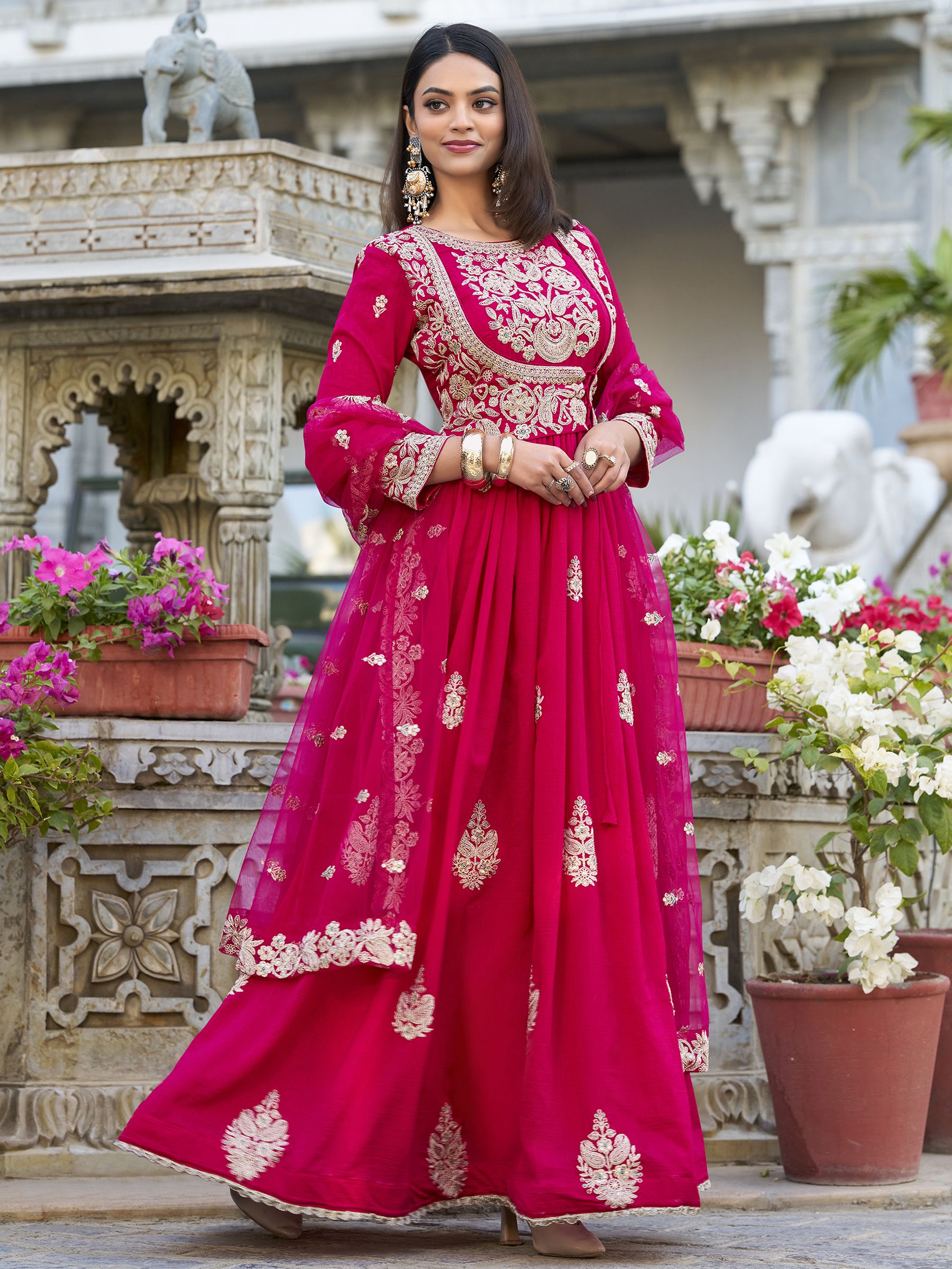 Anwitha Pink Embroidered Silk Anarkali Gown Set, crafted from luxurious Vichitra Silk with intricate sequins and thread embroidery accented by delicate lace details. This fully stitched Anarkali gown features a 3-meter flair and a soft cotton lining for comfort. Paired with a graceful net dupatta adorned with sequins embroidery and a lace border, this elegant ensemble is perfect for weddings, festive occasions, and grand celebrations