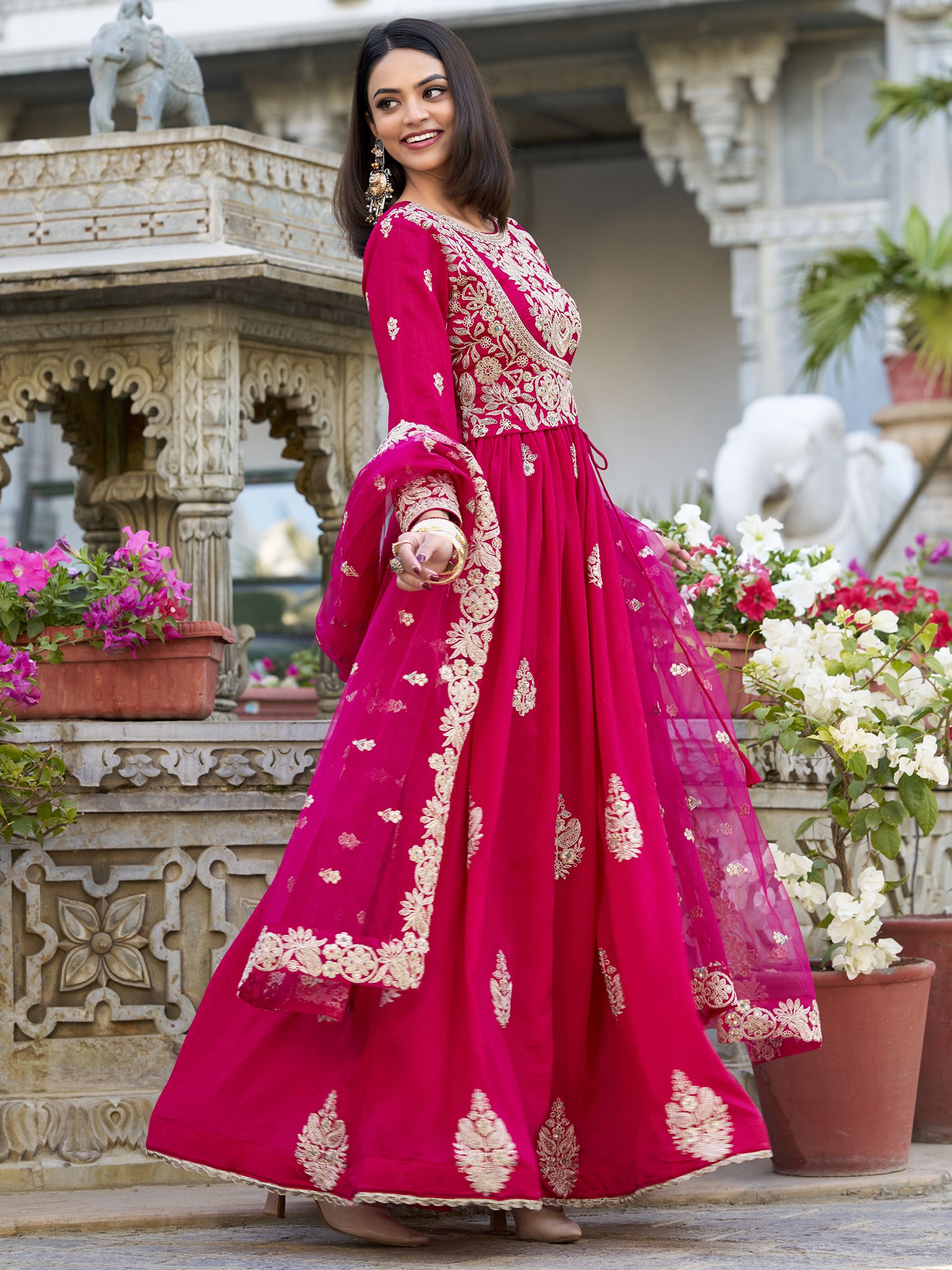 Anwitha Pink Embroidered Silk Anarkali Gown Set, crafted from luxurious Vichitra Silk with intricate sequins and thread embroidery accented by delicate lace details. This fully stitched Anarkali gown features a 3-meter flair and a soft cotton lining for comfort. Paired with a graceful net dupatta adorned with sequins embroidery and a lace border, this elegant ensemble is perfect for weddings, festive occasions, and grand celebrations