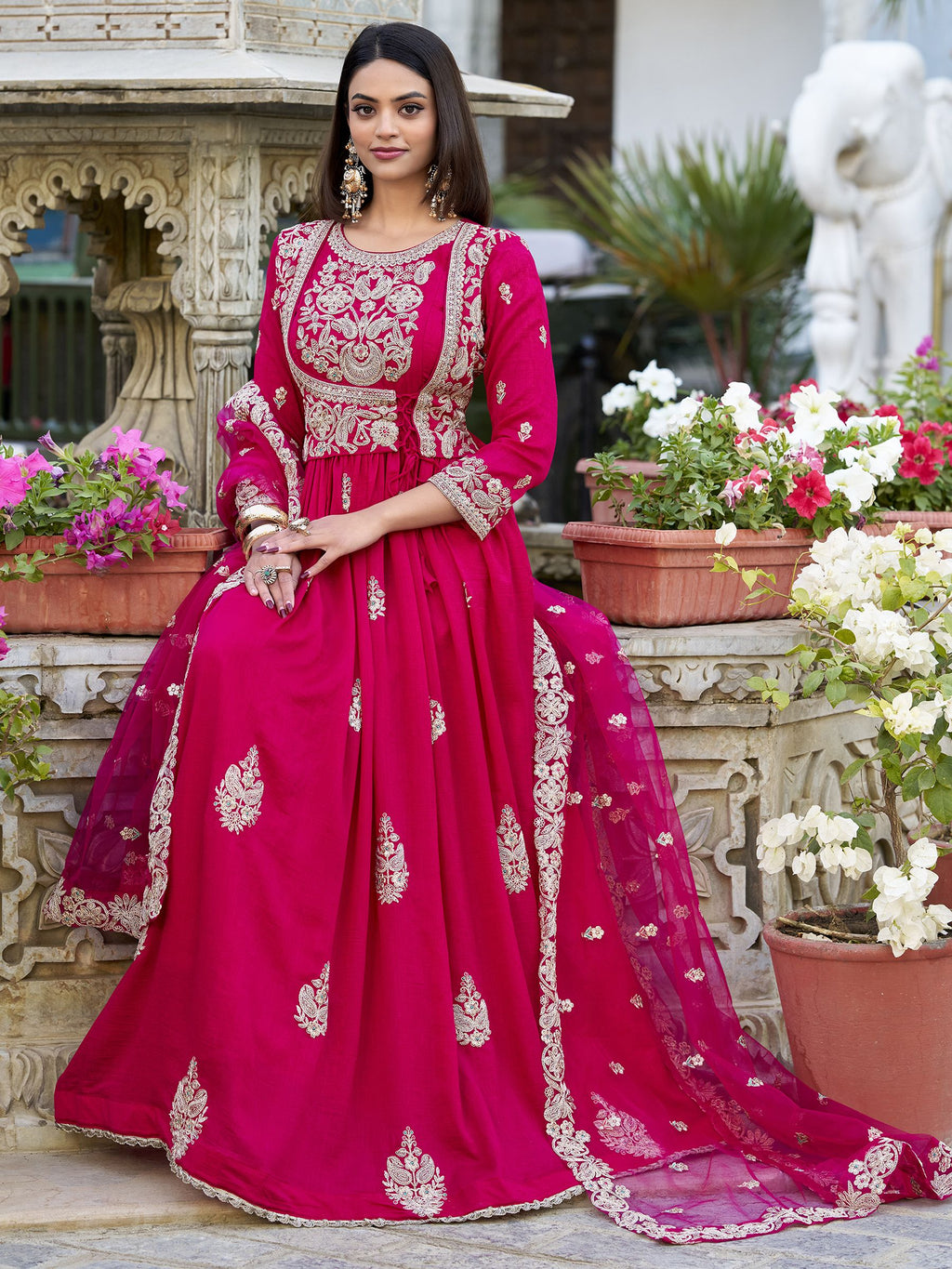 Anwitha Pink Embroidered Silk Anarkali Gown Set, crafted from luxurious Vichitra Silk with intricate sequins and thread embroidery accented by delicate lace details. This fully stitched Anarkali gown features a 3-meter flair and a soft cotton lining for comfort. Paired with a graceful net dupatta adorned with sequins embroidery and a lace border, this elegant ensemble is perfect for weddings, festive occasions, and grand celebrations