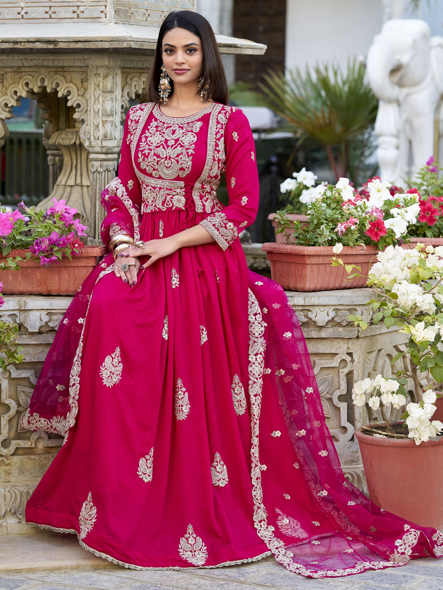 Anwitha Pink Embroidered Silk Anarkali Gown Set, crafted from luxurious Vichitra Silk with intricate sequins and thread embroidery accented by delicate lace details. This fully stitched Anarkali gown features a 3-meter flair and a soft cotton lining for comfort. Paired with a graceful net dupatta adorned with sequins embroidery and a lace border, this elegant ensemble is perfect for weddings, festive occasions, and grand celebrations