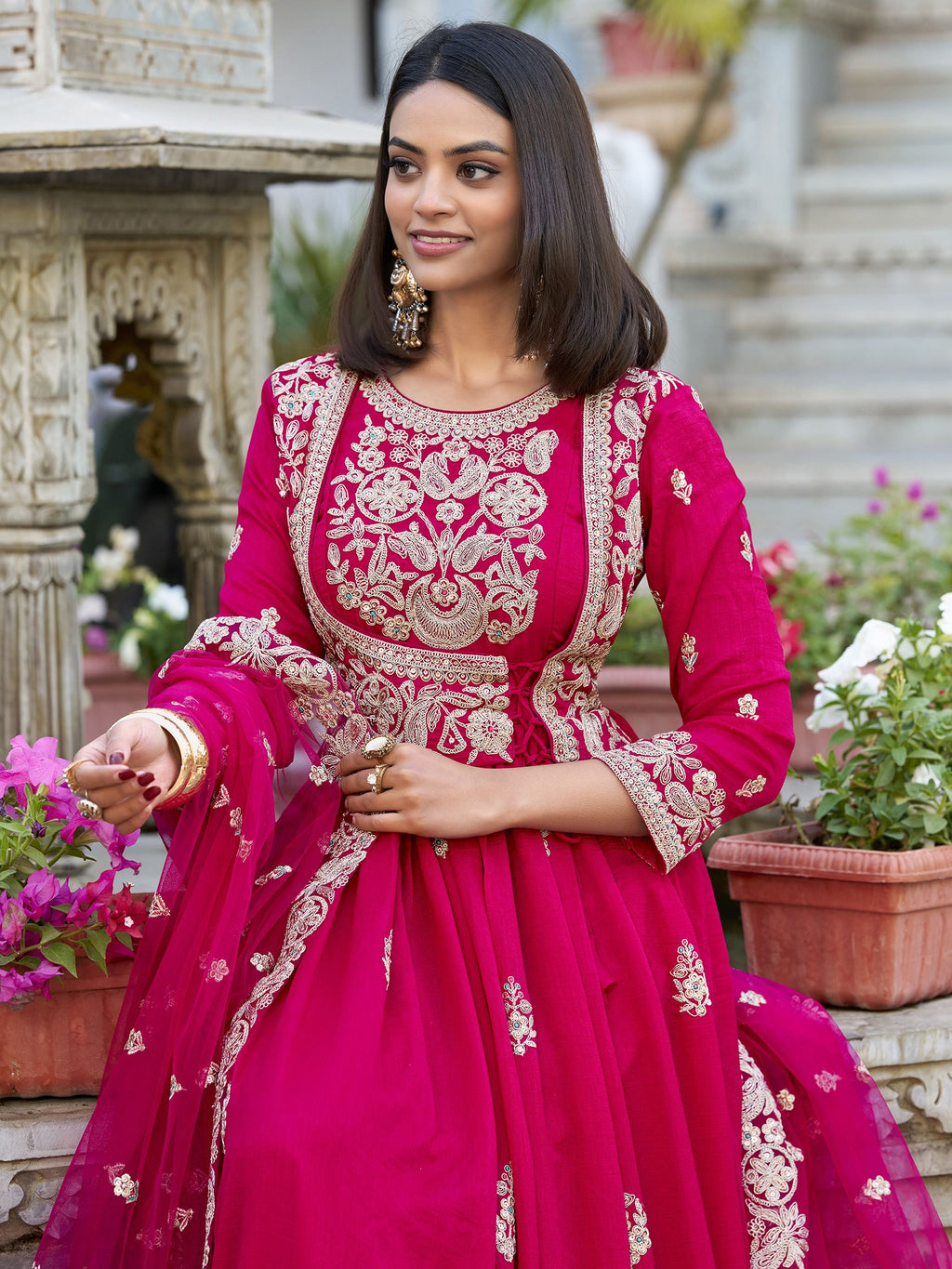 Anwitha Pink Embroidered Silk Anarkali Gown Set, crafted from luxurious Vichitra Silk with intricate sequins and thread embroidery accented by delicate lace details. This fully stitched Anarkali gown features a 3-meter flair and a soft cotton lining for comfort. Paired with a graceful net dupatta adorned with sequins embroidery and a lace border, this elegant ensemble is perfect for weddings, festive occasions, and grand celebrations