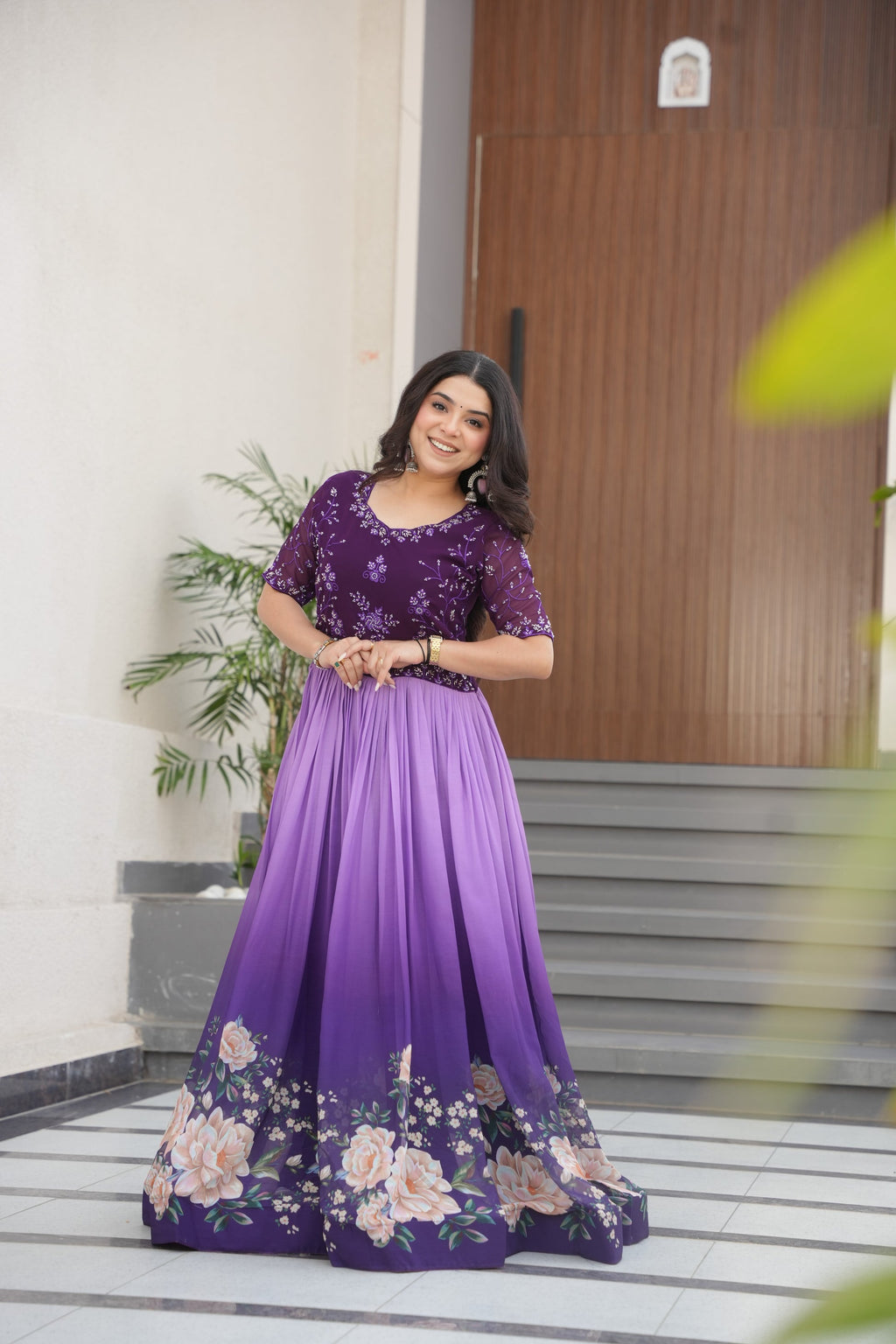 Hemrika Purple Embroidered Gown – elegant purple ethnic gown for women with floral print and beads embroidery, floor-length faux blooming gown, half sleeve gown with round neckline, canvas patta stitched Anarkali style gown, partywear gown for weddings and festive occasions, Indian designer gown with cotton lining, stylish readymade ethnic gown by Trinaari.