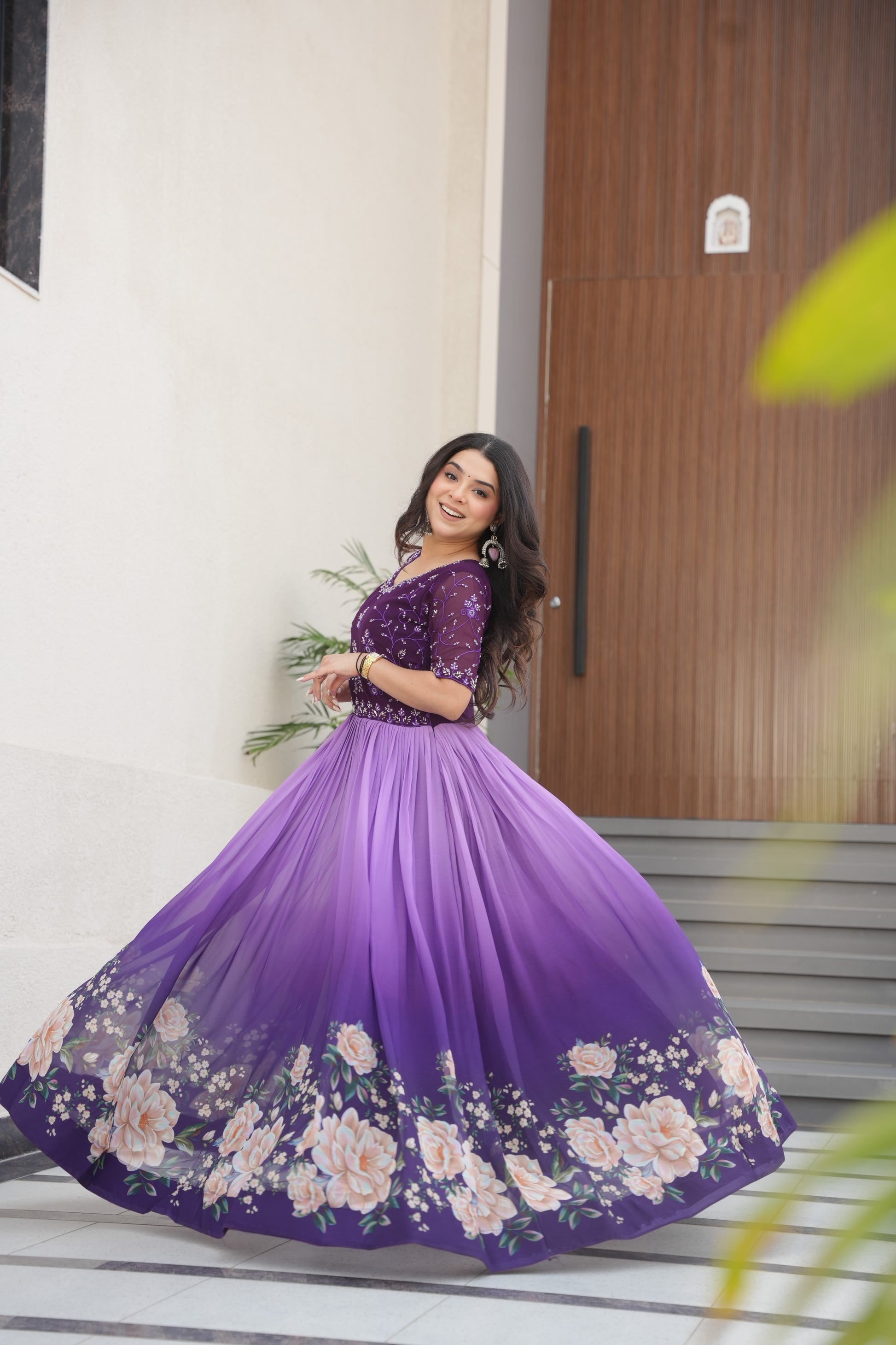 Hemrika Purple Embroidered Gown – elegant purple ethnic gown for women with floral print and beads embroidery, floor-length faux blooming gown, half sleeve gown with round neckline, canvas patta stitched Anarkali style gown, partywear gown for weddings and festive occasions, Indian designer gown with cotton lining, stylish readymade ethnic gown by Trinaari.