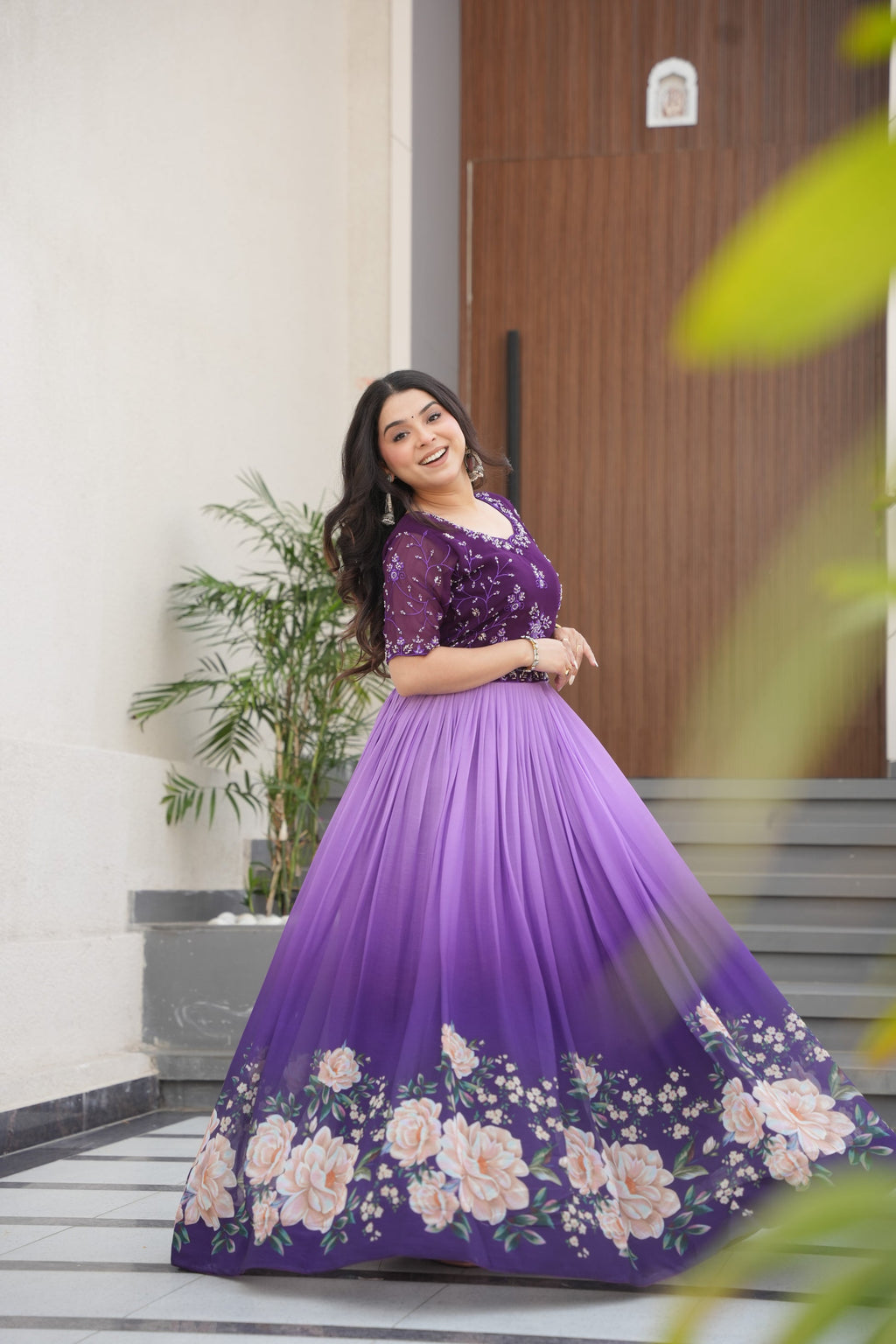 Hemrika Purple Embroidered Gown – elegant purple ethnic gown for women with floral print and beads embroidery, floor-length faux blooming gown, half sleeve gown with round neckline, canvas patta stitched Anarkali style gown, partywear gown for weddings and festive occasions, Indian designer gown with cotton lining, stylish readymade ethnic gown by Trinaari.