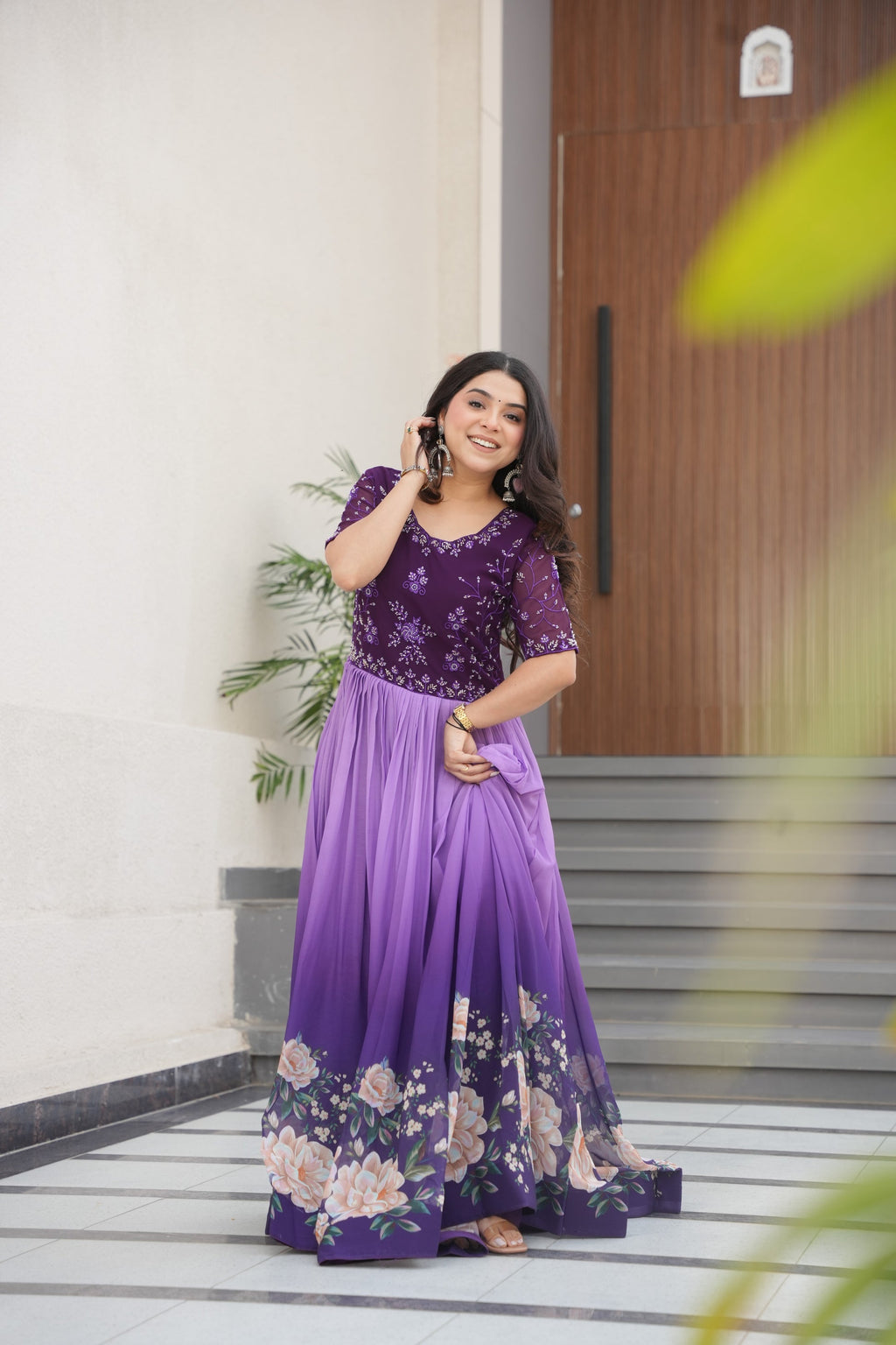Hemrika Purple Embroidered Gown – elegant purple ethnic gown for women with floral print and beads embroidery, floor-length faux blooming gown, half sleeve gown with round neckline, canvas patta stitched Anarkali style gown, partywear gown for weddings and festive occasions, Indian designer gown with cotton lining, stylish readymade ethnic gown by Trinaari.