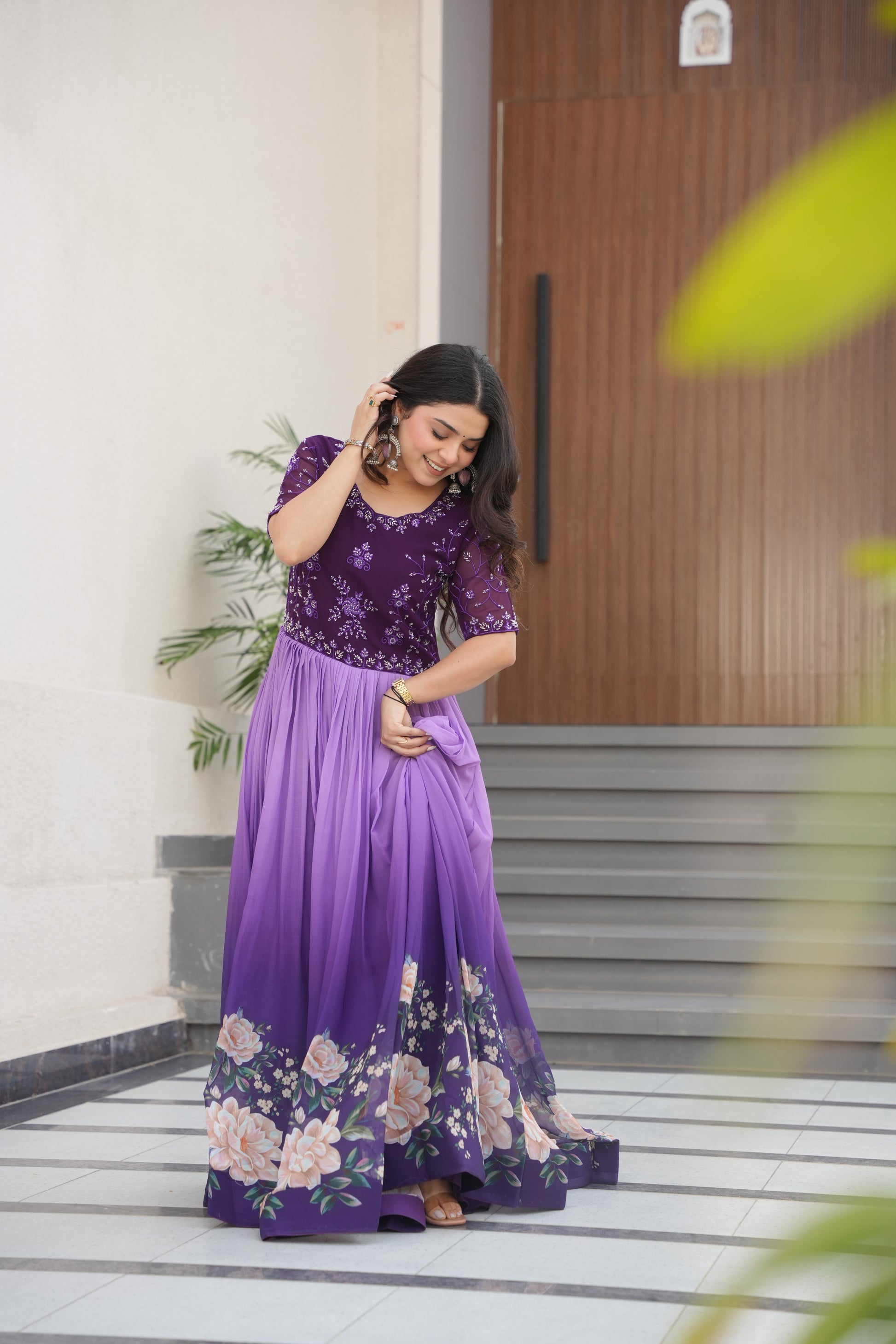 Hemrika Purple Embroidered Gown – elegant purple ethnic gown for women with floral print and beads embroidery, floor-length faux blooming gown, half sleeve gown with round neckline, canvas patta stitched Anarkali style gown, partywear gown for weddings and festive occasions, Indian designer gown with cotton lining, stylish readymade ethnic gown by Trinaari.