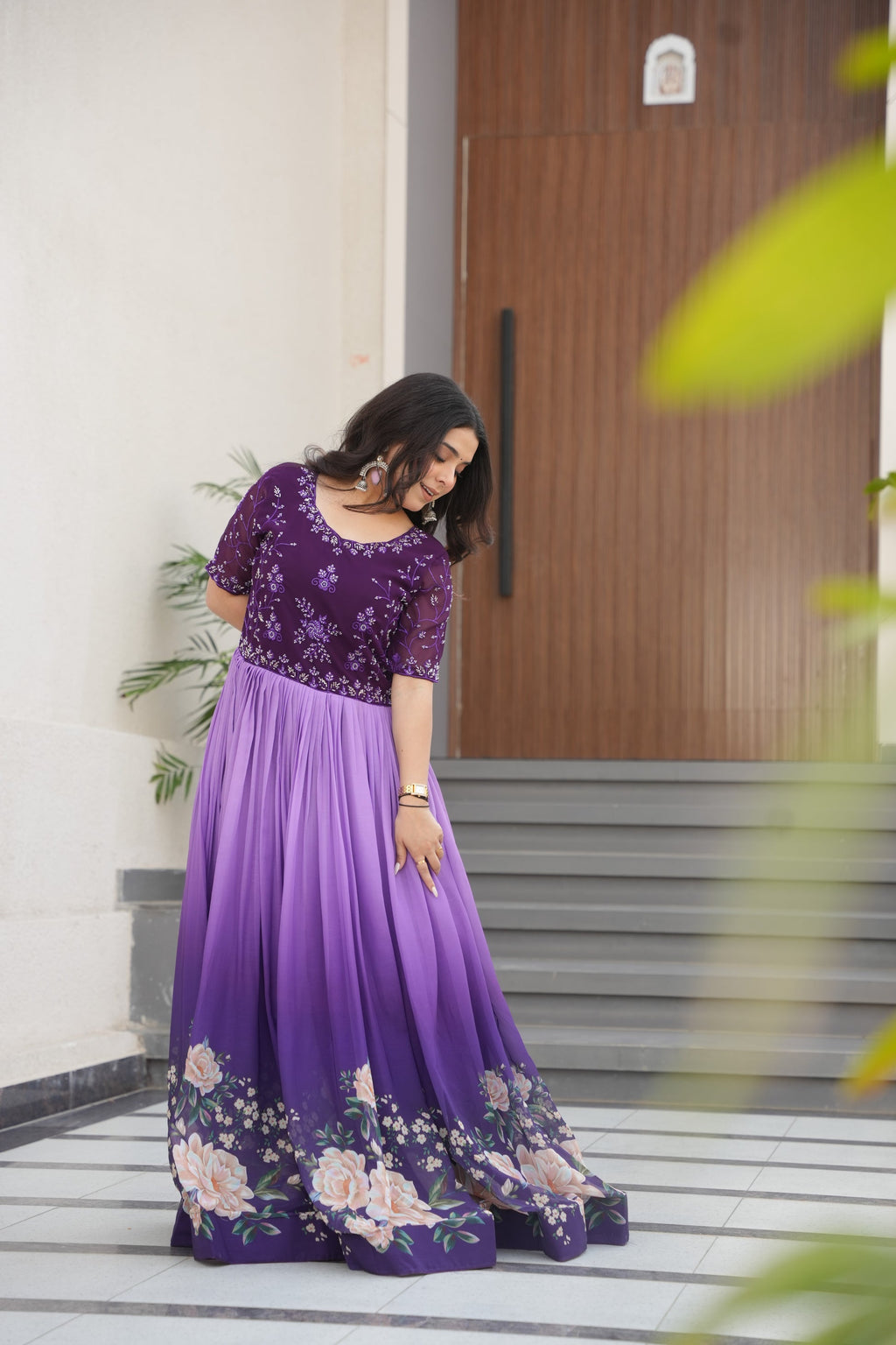 Hemrika Purple Embroidered Gown – elegant purple ethnic gown for women with floral print and beads embroidery, floor-length faux blooming gown, half sleeve gown with round neckline, canvas patta stitched Anarkali style gown, partywear gown for weddings and festive occasions, Indian designer gown with cotton lining, stylish readymade ethnic gown by Trinaari.