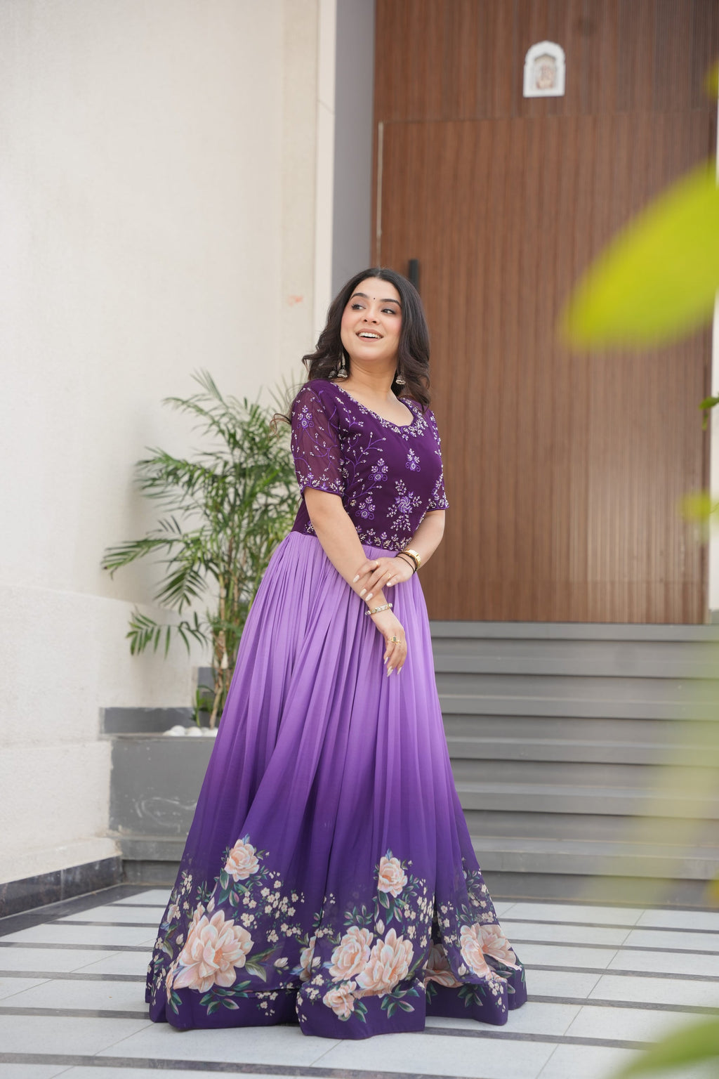 Hemrika Purple Embroidered Gown – elegant purple ethnic gown for women with floral print and beads embroidery, floor-length faux blooming gown, half sleeve gown with round neckline, canvas patta stitched Anarkali style gown, partywear gown for weddings and festive occasions, Indian designer gown with cotton lining, stylish readymade ethnic gown by Trinaari.