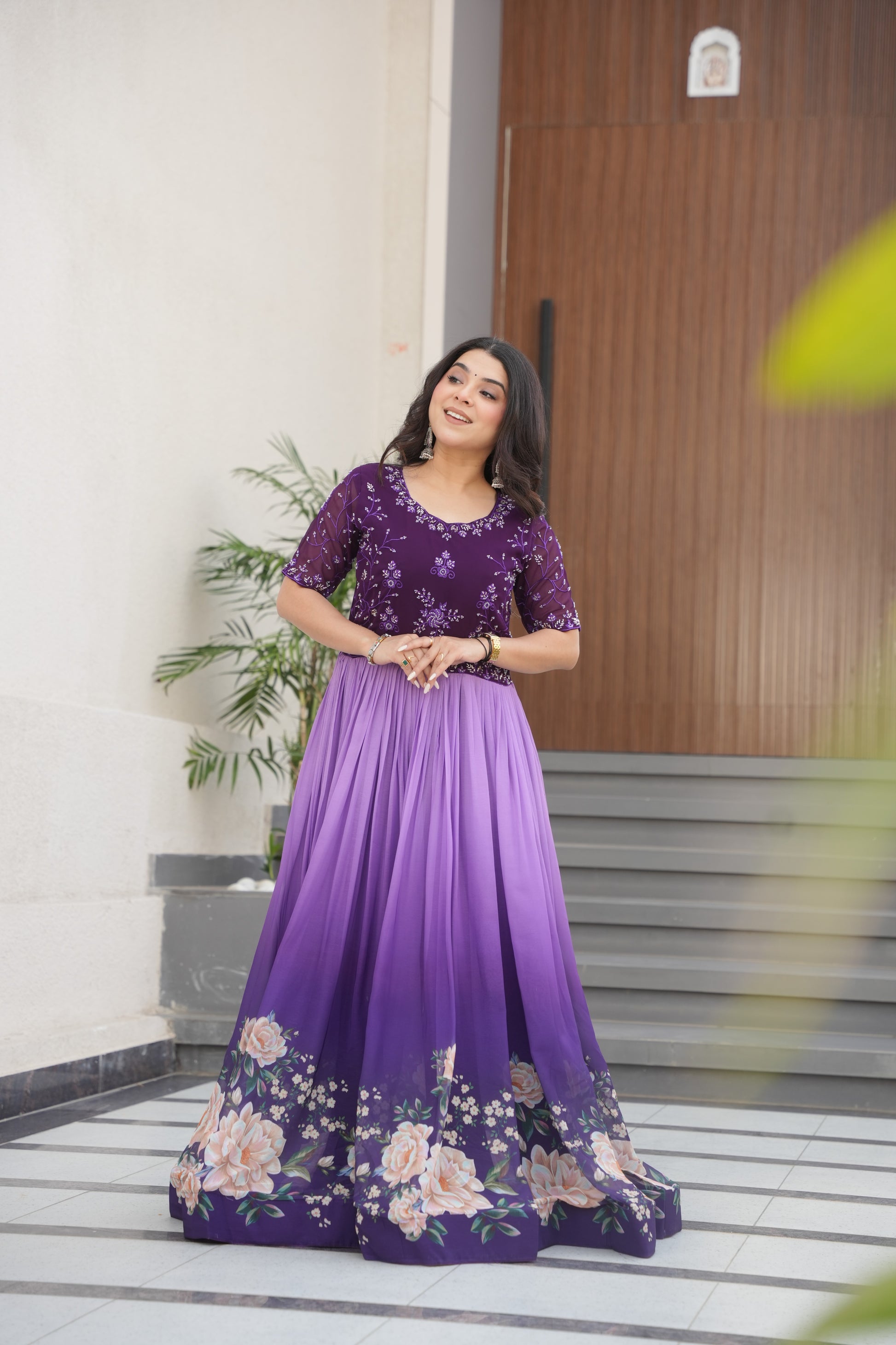 Hemrika Purple Embroidered Gown – elegant purple ethnic gown for women with floral print and beads embroidery, floor-length faux blooming gown, half sleeve gown with round neckline, canvas patta stitched Anarkali style gown, partywear gown for weddings and festive occasions, Indian designer gown with cotton lining, stylish readymade ethnic gown by Trinaari.