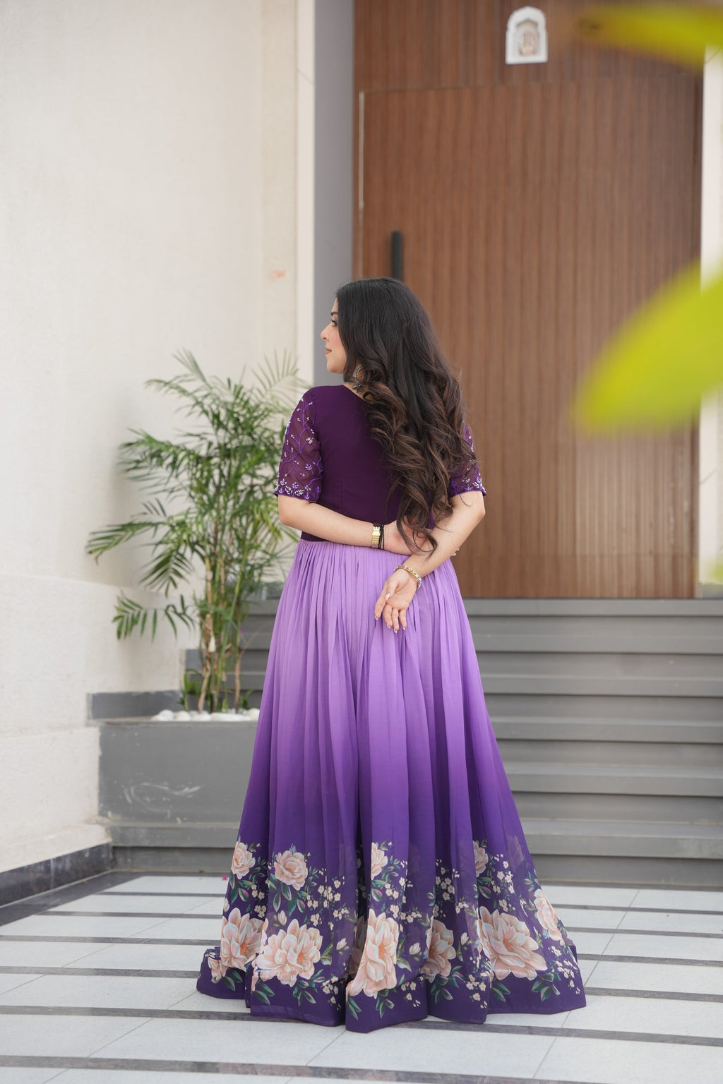 Hemrika Purple Embroidered Gown – elegant purple ethnic gown for women with floral print and beads embroidery, floor-length faux blooming gown, half sleeve gown with round neckline, canvas patta stitched Anarkali style gown, partywear gown for weddings and festive occasions, Indian designer gown with cotton lining, stylish readymade ethnic gown by Trinaari.