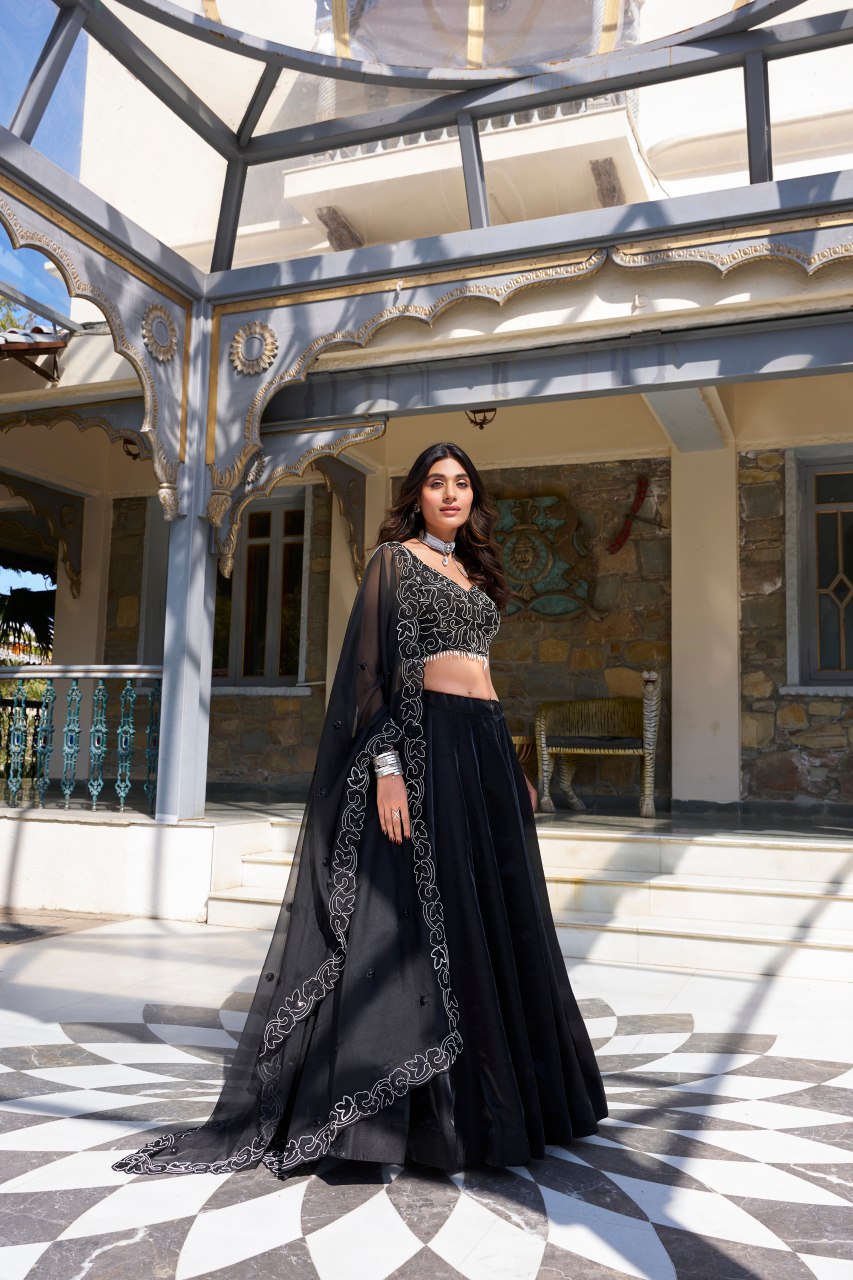 Varnisha Black Designer Lehenga Choli crafted from premium star satin fabric, featuring a sleek plain lehenga with a voluminous 4.80-meter flair, stitched with canvas and can-can for structure. The unstitched blouse showcases intricate pearl coding and sequins embroidery, while the matching star satin dupatta is adorned with sequins work and a lace border. Perfect for wedding receptions, cocktail parties, and festive occasions, this elegant ensemble exudes luxury and timeless style