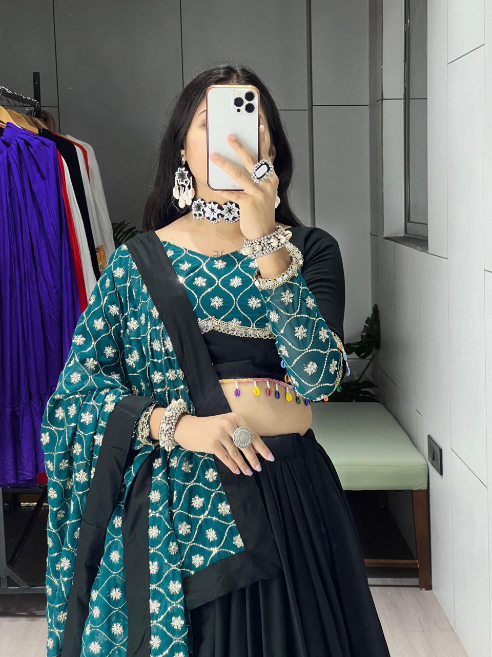 Person wearing a green and black traditional outfit with jewelry, taking a mirror selfie.