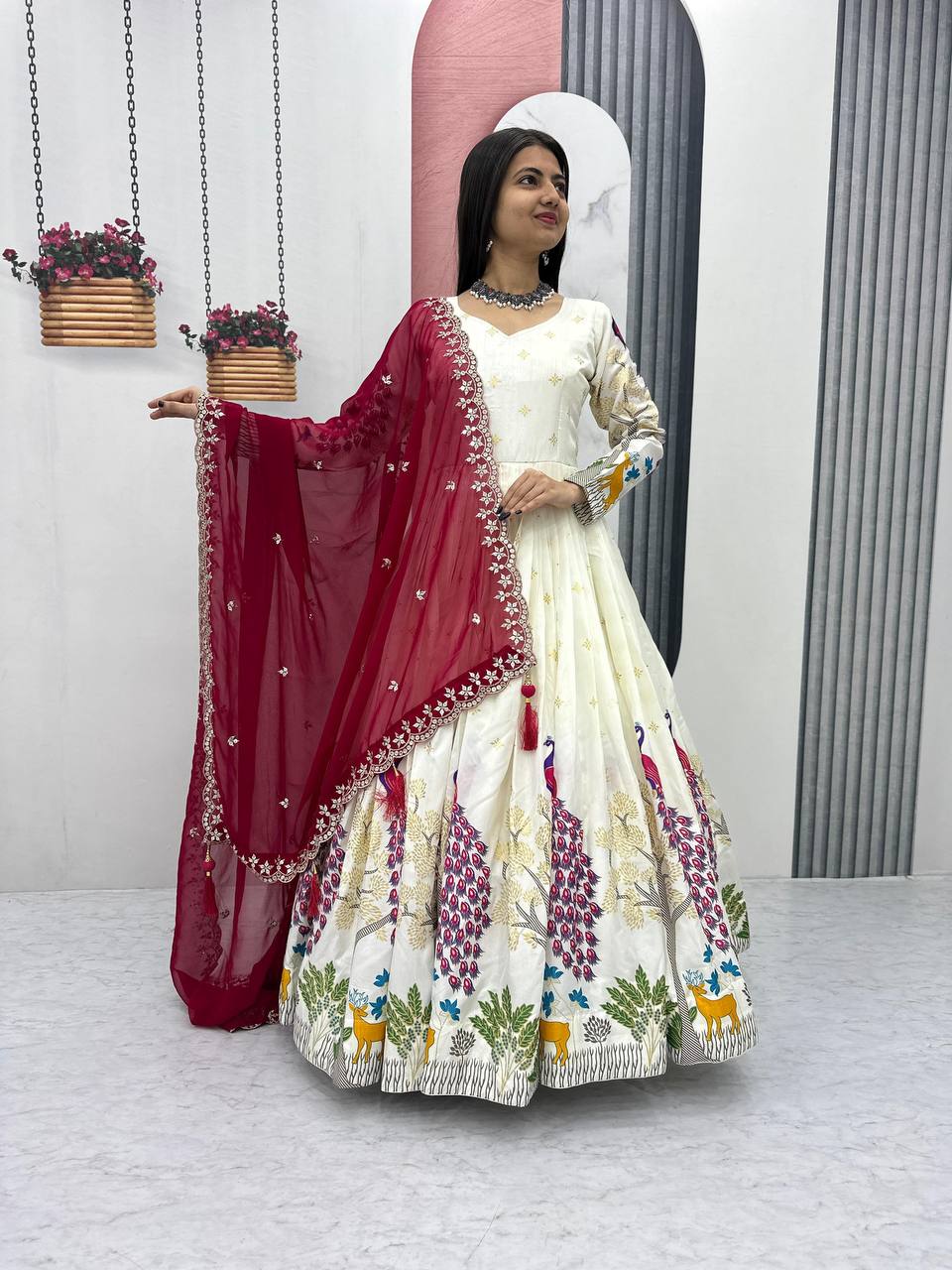 Tarini White Dola Silk Anarkali Gown Set featuring a mesmerizing peacock design with intricate mill print and foil work. Made from premium Dola Silk with a 3-meter flair, it comes with a fully stitched gown and a beautifully embroidered Fox Georgette dupatta adorned with heavy 7mm sequins embroidery. Perfect for festive occasions, weddings, and celebrations, this elegant ensemble blends traditional craftsmanship with contemporary charm