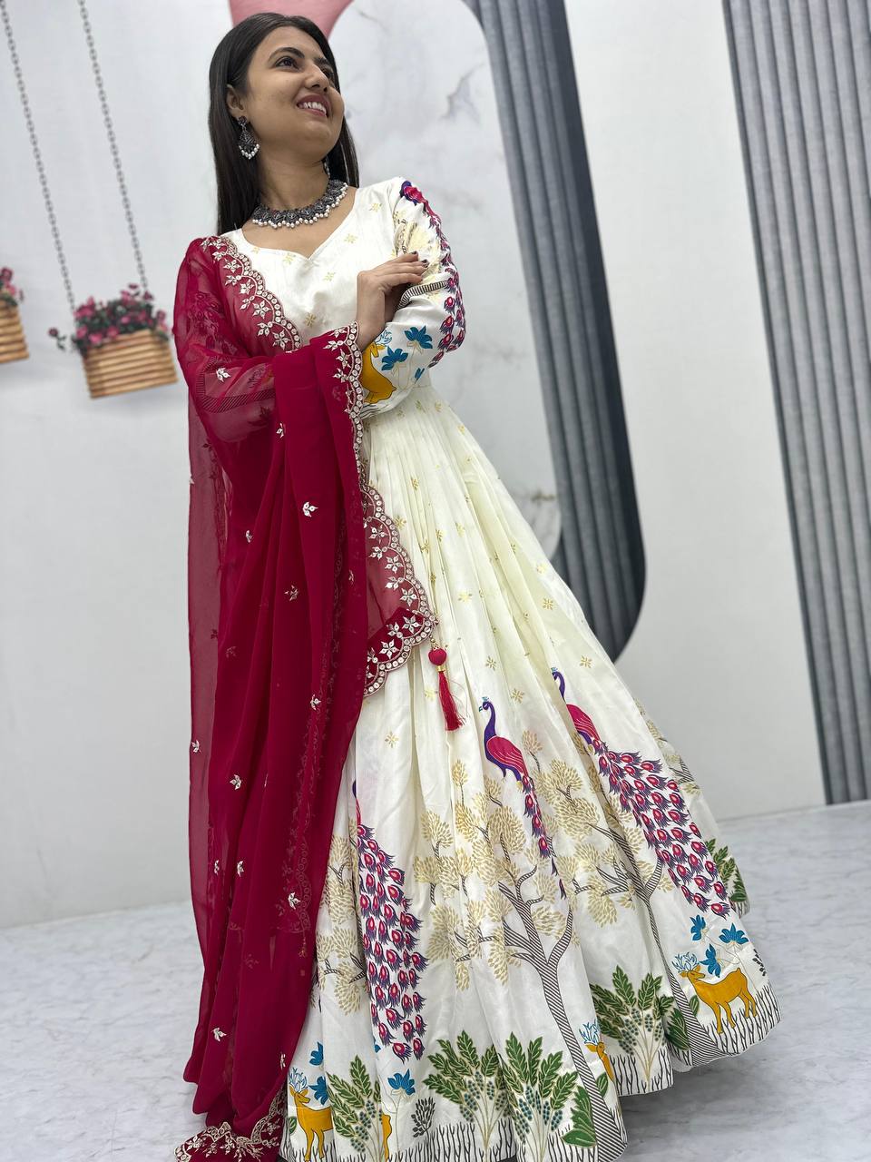 Tarini White Dola Silk Anarkali Gown Set featuring a mesmerizing peacock design with intricate mill print and foil work. Made from premium Dola Silk with a 3-meter flair, it comes with a fully stitched gown and a beautifully embroidered Fox Georgette dupatta adorned with heavy 7mm sequins embroidery. Perfect for festive occasions, weddings, and celebrations, this elegant ensemble blends traditional craftsmanship with contemporary charm