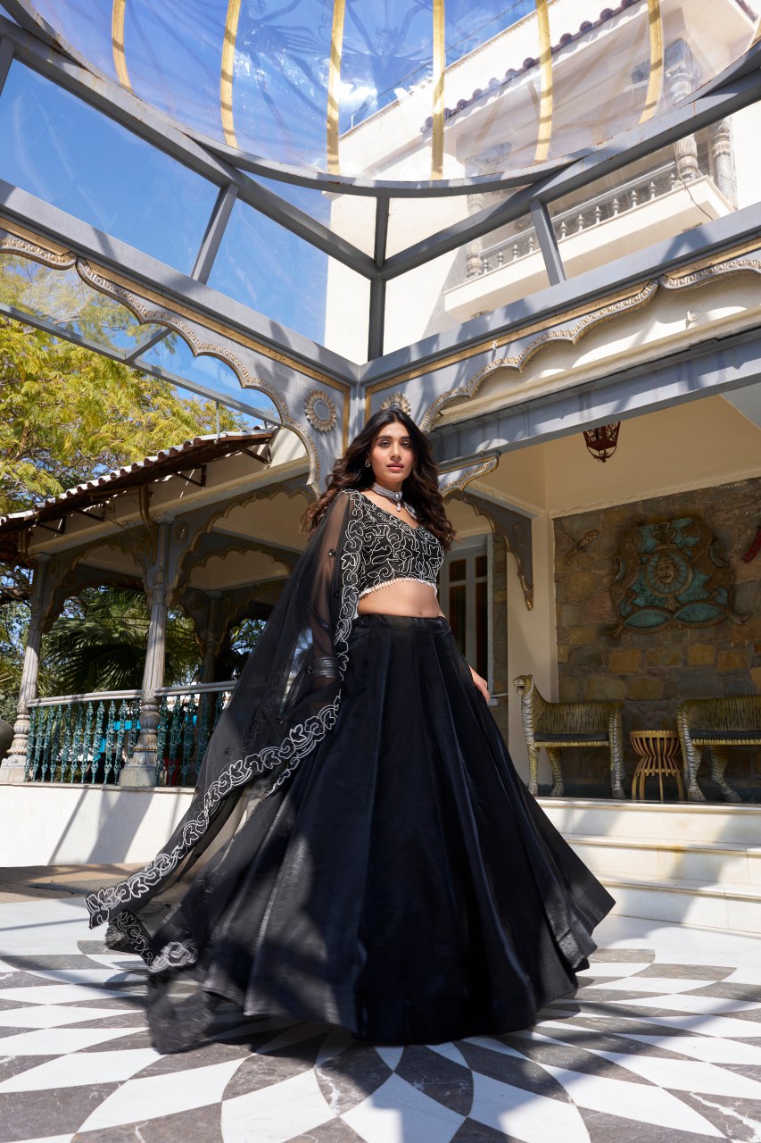 Varnisha Black Designer Lehenga Choli crafted from premium star satin fabric, featuring a sleek plain lehenga with a voluminous 4.80-meter flair, stitched with canvas and can-can for structure. The unstitched blouse showcases intricate pearl coding and sequins embroidery, while the matching star satin dupatta is adorned with sequins work and a lace border. Perfect for wedding receptions, cocktail parties, and festive occasions, this elegant ensemble exudes luxury and timeless style