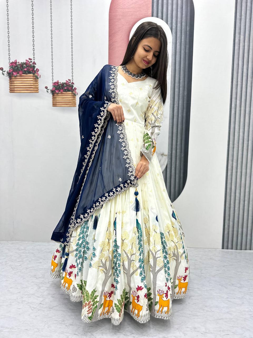 Tarini White Dola Silk Anarkali Gown Set featuring a mesmerizing peacock design with intricate mill print and foil work. Made from premium Dola Silk with a 3-meter flair, it comes with a fully stitched gown and a beautifully embroidered Fox Georgette dupatta adorned with heavy 7mm sequins embroidery. Perfect for festive occasions, weddings, and celebrations, this elegant ensemble blends traditional craftsmanship with contemporary charm