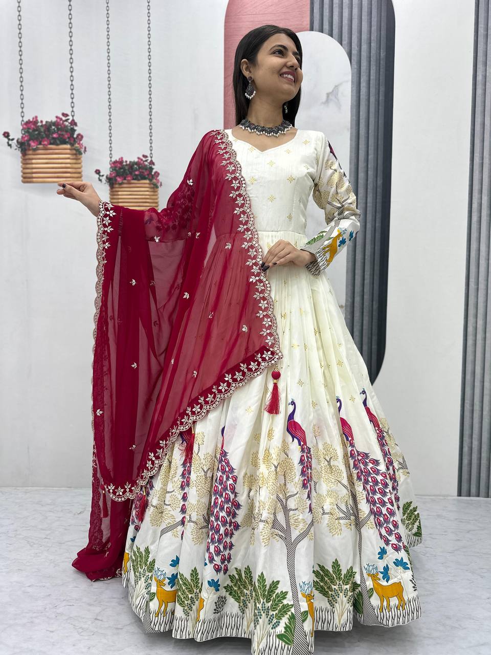 Tarini White Dola Silk Anarkali Gown Set featuring a mesmerizing peacock design with intricate mill print and foil work. Made from premium Dola Silk with a 3-meter flair, it comes with a fully stitched gown and a beautifully embroidered Fox Georgette dupatta adorned with heavy 7mm sequins embroidery. Perfect for festive occasions, weddings, and celebrations, this elegant ensemble blends traditional craftsmanship with contemporary charm