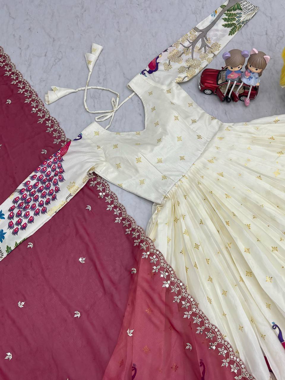 Tarini White Dola Silk Anarkali Gown Set featuring a mesmerizing peacock design with intricate mill print and foil work. Made from premium Dola Silk with a 3-meter flair, it comes with a fully stitched gown and a beautifully embroidered Fox Georgette dupatta adorned with heavy 7mm sequins embroidery. Perfect for festive occasions, weddings, and celebrations, this elegant ensemble blends traditional craftsmanship with contemporary charm